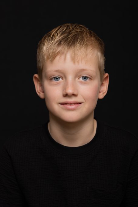 Jongen met blond haar, recht in de camera kijkend, op een zwarte achtergrond.
